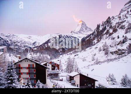 Ein malerischer Blick auf das schneegeschmückte Bergdorf Zermatt mit dem Matterhorn, das bei Sonnenaufgang vor einer Winterlandschaft leuchtet. Stockfoto