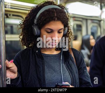 Frau mit Headset in der U-Bahn Junge Erwachsene Frau mit Headset und Smartphone Musik auf dem Weg mit der U-Bahn. New York City, New York, USA. New York City Subway Train, Manhattan New York Vereinigte Staaten von Amerika Copyright: XGuidoxKoppesxPhotox Stockfoto
