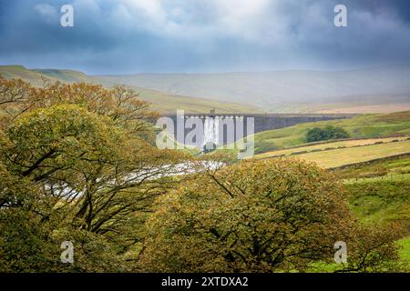 Das Wasser kaskadiert über eine Angram-Staumauer mit herbstlichen Bäumen im Vordergrund Stockfoto