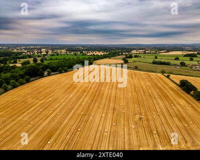 Die weitläufige Luftperspektive zeigt goldene Felder mit Strohballen in üppiger grüner Umgebung. Stockfoto