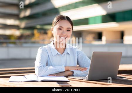 Junger Profi lächelt beim Arbeiten an einem Laptop im urbanen Outdoor Stockfoto