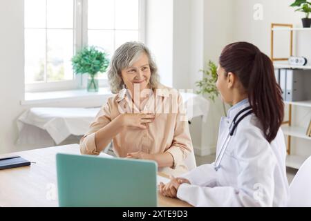 Ältere Patientin sitzt am Schreibtisch in der Arztpraxis und spricht mit einer jungen Ärztin. Stockfoto