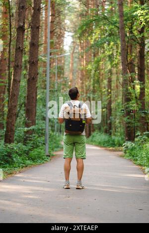 Mann mit Rucksack geht auf einem Waldweg, umgeben von hohen Bäumen, und genießt eine friedliche Wanderung in der Natur. Eine Tour durch den Kiefernwald. Stockfoto