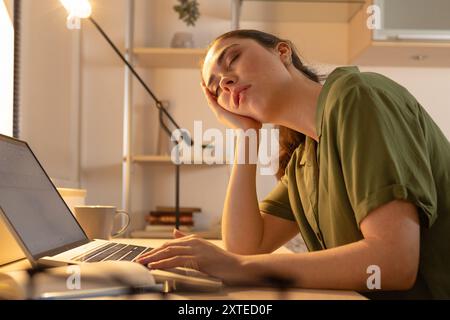 Nahaufnahme einer müden jungen Frau sitzt mit einem Laptop an ihrem Schreibtisch und schläft ein. Ermüdung durch Überlastung. Der Schüler schläft in der Nähe des Compu ein Stockfoto