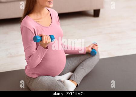 Nicht erkennbare schwangere Frau mit Kurzhanteln auf Yoga Matte Stockfoto