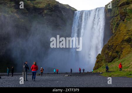 Skogafoss, Island, 16.05.2022. Blick auf den Skogafoss-Wasserfall mit Wasserspray und Menschen in farbenfrohen Jacken, die unten laufen. Stockfoto