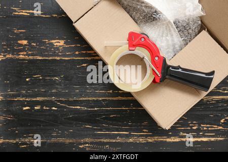 Abroller für Verpackungsband und Karton auf schwarzem Holzhintergrund Stockfoto