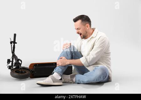 Gutaussehender Mann fiel vom Elektroroller auf hellem Hintergrund Stockfoto