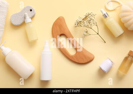 Komposition mit hölzernem guasha-Körpermassagewerkzeug und Flaschen kosmetischer Produkte auf beigem Hintergrund, Nahaufnahme Stockfoto