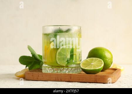 Holztablett mit Glas leckerer Limonade, Minze und Limetten auf weißem Hintergrund Stockfoto