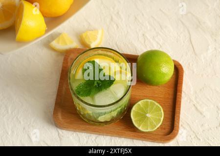 Holztablett mit Glas leckerer Limonade, Zitronen und Limetten auf weißem Hintergrund Stockfoto