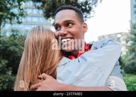 Ein junger Afroamerikaner umarmt seine Freundin. Multirassisches Paar, das glücklich umarmt. Freund und Freundin grüßen einander bei einem Date. Zwei Teenager, die sich zusammen umarmen. Hochwertige Fotos Stockfoto