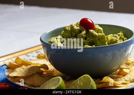 Guacamole in einer blauen Schüssel mit einer Kirschtomate darauf umgeben von Nachos. Stockfoto