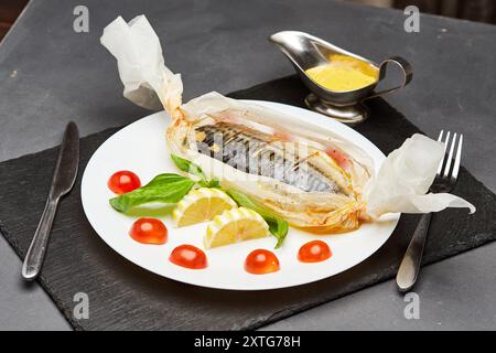 Gourmet gebackene Makrele in Pergament mit Zitronenscheiben, Basilikum und Kirschtomaten Stockfoto