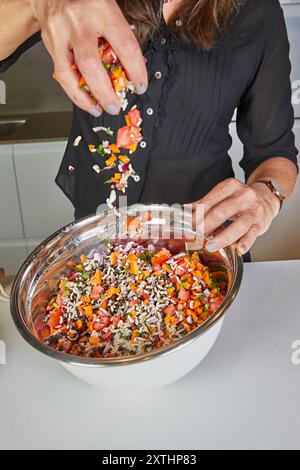 Nahaufnahme einer Person, die gemahlene Gewürze über einen bunten Salat in einer Edelstahlschüssel in der Küche streut. Stockfoto