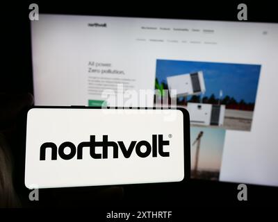 Person mit Smartphone und Logo des schwedischen Batterieunternehmens Northvolt ab vor der Website. Schwerpunkt auf dem Display des Telefons. Stockfoto