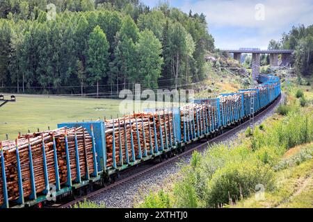 Fenniarail Oy Lokomotive, die einen langen Güterzug mit Eisenbahnwaggons voller Zellstoffholz zur Mühle zieht, Rückansicht. Salo, Finnland. August 2024. Stockfoto