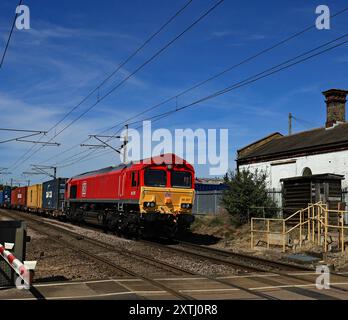 Die DB Cargo-Diesellokomotive Nr. 66207 mit Güterzug überquert einen Bahnübergang und das Gelände des ehemaligen Bahnhofs Haughley in Suffolk Stockfoto