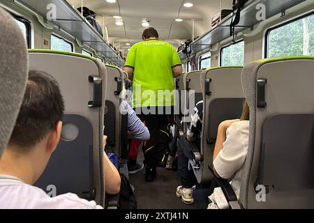 27.07.2024, Berlin, DE - Zugbegleiter im Abteil eines Flixtrain. Alltag, Bahn, Bahnreise, Bahnverkehr, befoerdern, Befoerderung, Berlin, Beruf, Berufsalltag, deutsch, Deutschland, Eisenbahn, Europa, Europa, Fahrgaeste, Fernverkehr, Fernzug, Flix Train, Flixtrain, Gesellschaft, Großraumwagen, innen, Innenaufnahme, Job, Kaukasier, Kaukasisch, Menschen, Personal, Personen, Personenbeförderung, Personenfernverkehr, Personentransport, QF, Querformat, Reise, Reisen, Rueckansicht, Schienenverkehr, Servicekraft, Sitze, Sitzplaetze, Sitzreihen, Transport, Verkehr, Waggon, Westeuropa, Wirtschaft Stockfoto