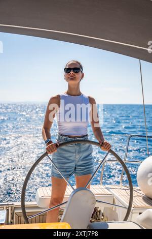 Die junge weibliche Kapitänin steht am Ruder und kontrolliert ein Segelboot während einer Fahrt auf dem Seeweg Stockfoto