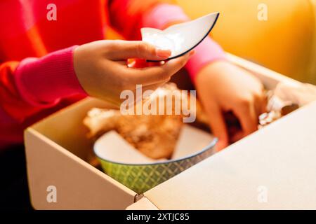 Ein Afrikaner packt eine Pappschachtel im Wohnzimmer des Hauses aus. Ein bezauberndes schwarzes Mädchen ist empört über einen gebrochenen Teller. Eine attraktive junge Frau in Stockfoto