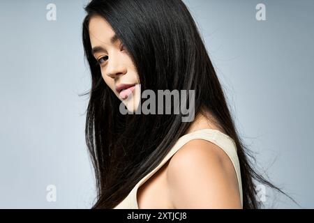 Eine junge Frau mit langen schwarzen Haaren schlägt eine stilvolle Pose vor einem hellblauen Hintergrund. Stockfoto