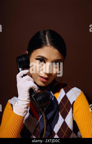 Eine junge Frau in einem modischen Pullover hält ein Vintage-Drehtelefon, ihr Ausdruck faszinierend. Stockfoto