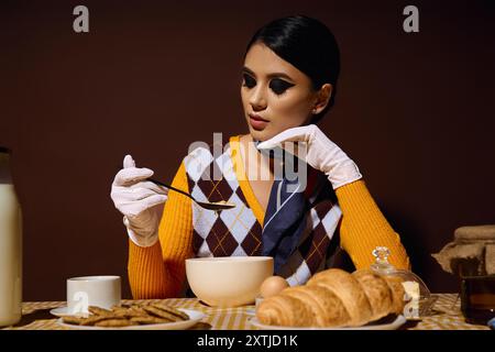 Eine junge Frau, die in stilvoller Retro-Kleidung gekleidet ist, genießt ein Frühstück mit Suppe und Gebäck. Stockfoto