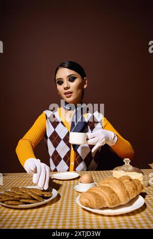 Stilvolle Frau sitzt mit Tee und Gebäck am Tisch und genießt das Frühstück. Stockfoto