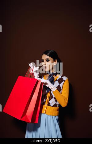 Eine modische junge Frau in einem gelben Pullover schaut aufgeregt auf Einkaufstaschen in ihren Händen. Stockfoto