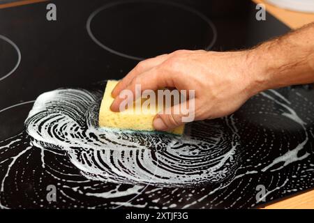 Nahaufnahme von männlichen Händen, die eine schwarze Glas-Kochfeldoberfläche reinigen. Stockfoto