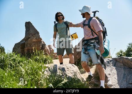 Ein junges Schwulenpaar macht eine Sommerwanderung Hand in Hand, während sie sich durch felsiges Gelände bewegen. Stockfoto