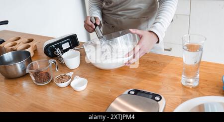 Home Backküche mit Zutaten und Utensilien auf hölzerner Arbeitsplatte, Person mischt Teig in Glasschale Stockfoto