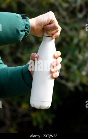 Der Mann hält eine Modell-Thermoskanne gegen verschwommene Büsche aus der Nähe Stockfoto