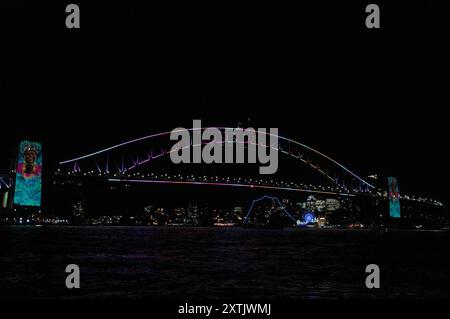 Sydneys Wahrzeichen, die Harbour Bridge, beleuchtet mit farbigen lazar-Lichtern und Aborigines-Kunstbanner, die an den Brückensäulen hängen, nahmen an der A Teil Stockfoto