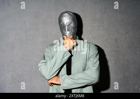 Geheimnisvoller, nachdenklicher Mann mit Klebeband Gesicht, der Arm am Kinn über grauem Hintergrund denkt Stockfoto
