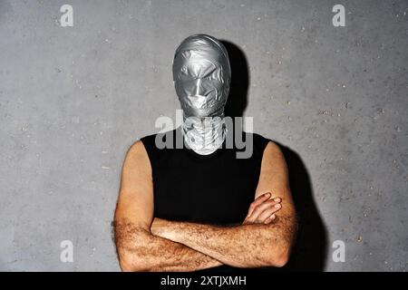 Mystery man mit Klebeband Gesichtspflege mit gekreuzten Armen auf grauem Hintergrund Stockfoto