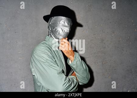 Geheimnisvoller, nachdenklicher Mann mit Klebeband Gesicht, der Arm am Kinn über grauem Hintergrund denkt Stockfoto