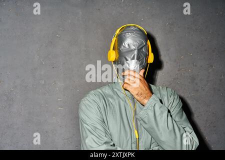 Mystery man mit Klebeband Gesicht tragen Kopfhörer hören Musik über grauem Hintergrund mit Kopierraum Stockfoto