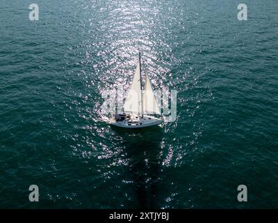 Ein ruhiges Segelboot gleitet auf ruhigem, tiefblauem Wasser unter klarem Himmel. Ferne Schiffe und Segelboote säumen den Horizont und schaffen eine friedliche Seefahrt Stockfoto