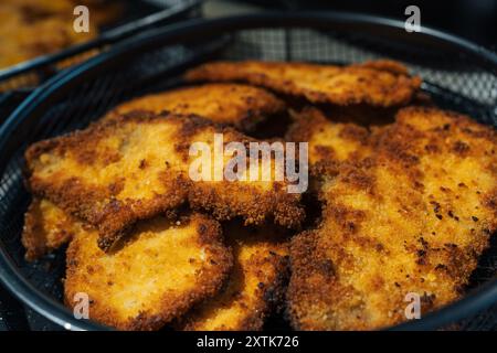 Korb gefüllt mit goldbraunen, knusprigen, hausgemachten, panierten Hühnchenkoteletts, frisch zubereitet und servierfertig. Die Nahaufnahme hebt die knusprige Textur und das köstliche Aussehen des Schnitzels hervor. Stockfoto