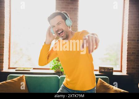 Foto-Porträt von gutaussehenden Reifen Mann Kopfhörer hören Musik tanzen Spaß gekleidet gelb Outfit gemütlich Tag Licht Haus innen Wohnzimmer Stockfoto