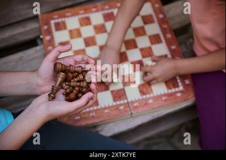 Eine Nahaufnahme von zwei Kindern, die an einem Schachspiel im Freien teilnehmen und strategisches Denken und Bildung durch ein hölzernes Schachbrett und Teile zeigen. Stockfoto