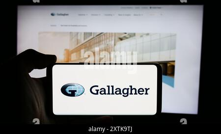 Person, die ein Mobiltelefon mit dem Logo des US-Versicherungsunternehmens Arthur J. Gallagher Co. (AJG) vor der Website des Unternehmens hält. Schwerpunkt auf dem Display des Telefons. Stockfoto