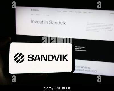 Person mit Smartphone und Logo des schwedischen Ingenieurunternehmens Sandvik ab vor der Website. Schwerpunkt auf dem Display des Telefons. Stockfoto