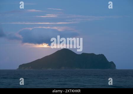 Nachts steigt der Mond langsam über Turtle Island auf, wo er plötzlich von Wolken verdeckt und dann dem ruhigen Wasser des Pazifischen Ozeans ausgesetzt wird. Stockfoto