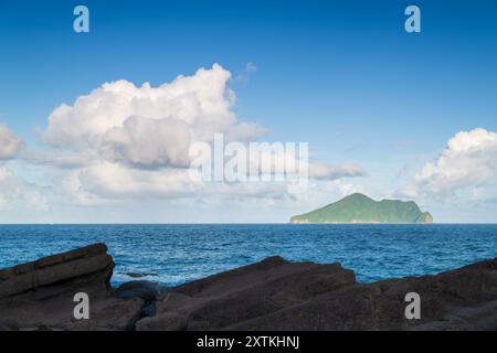 Eine ruhige Küstenlandschaft mit Schildkröteninsel am Horizont. Die Insel ist von einem riesigen blauen Ozean und einem flauschigen Himmel umgeben Stockfoto