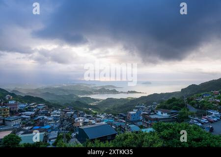 Von der Spitze des Berges aus entfaltet sich eine nebelbehüllte Landschaft, die ein malerisches Küstendorf inmitten sanfter Hügel zeigt. Jiufen, Taiwan. Stockfoto