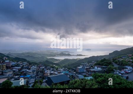 Von der Spitze des Berges aus entfaltet sich eine nebelbehüllte Landschaft, die ein malerisches Küstendorf inmitten sanfter Hügel zeigt. Jiufen, Taiwan. Stockfoto