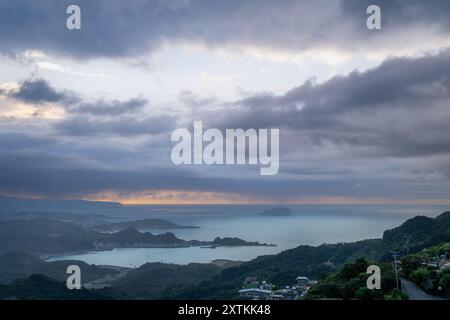 Von der Spitze des Berges aus entfaltet sich eine nebelbehüllte Landschaft, die ein malerisches Küstendorf inmitten sanfter Hügel zeigt. Jiufen, Taiwan. Stockfoto